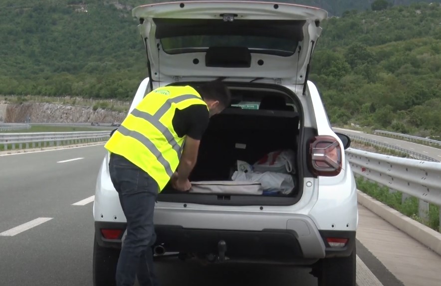 Vozač u zelenom prsluku vadi siguronosni troguao iz gepeka